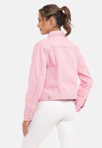 Roze denimjack met een cropped ontwerp, opvallende stiksels en drukknoopaccenten. De textuur van de stof suggereert duurzaamheid en structuur.