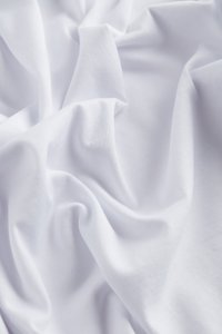 Witte katoenen stof die gedrapeerd en gekreukt is, met een gladde textuur en een lichte glans, met subtiele stiksels in de weving.