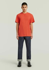 Camiseta de algodón roja con cuello redondo y manga corta, combinada con jeans de mezclilla oscura con puños doblados y zapatos negros.