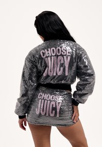 Ezüst flitteres bomber dzseki és miniszoknya szett. Fekete mandzsettákkal és nagy rózsaszín "CHOOSE JUICY" felirattal a háton és a szoknyán. Csillogó textúra.