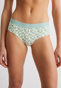 Culottes à motif floral vert avec une ceinture élastique bleu clair, présentant une texture lisse et une coupe ajustée.