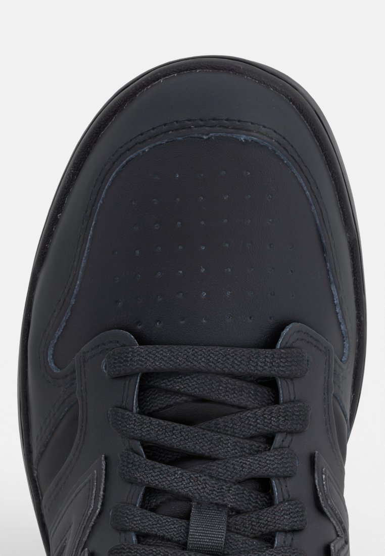 Chaussure de sport en cuir noir avec un bout arrondi, des détails perforés et des lacets plats. Accent de logo sur le côté et semelle en caoutchouc texturé.
