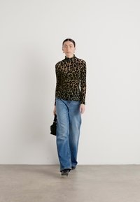Een turtleneck top met luipaardprint, bruin en zwart patroon, gecombineerd met lichtblauwe wijde jeans en een kleine zwarte handtas.