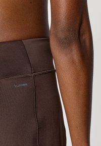 Καφέ αθλητικό κολάν με ομαλή υφή, με εμφανές ραφή κατά μήκος της πλευράς και ετικέτα "CLIMACOOL" κοντά στη μέση.