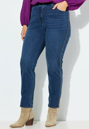 Mørkeblå denimjeans med lige pasform, der har sidesyninger og høj talje, sat sammen med beige ankelstøvler.