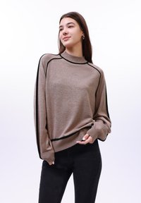 Barna kötött pulóver fekete részletekkel, magas gallérral, bordás mandzsettákkal és laza szabással. Az anyag puha megjelenésű, texturált felülettel.