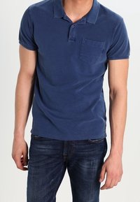 Marineblaues Poloshirt aus weicher Baumwolle mit einer drei-Knopf-Leiste, kurzen Ärmeln und einer aufgesetzten Tasche auf der linken Brust. Legere Passform.