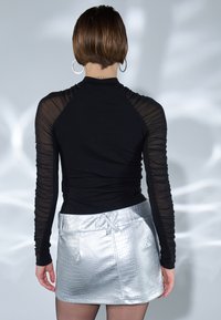 Svart langermet topp med gjennomsiktige, rynkete ermer; paired med en sølvfarget mini-skjørt i faux-krokodille med frontlommer og en blank finish.