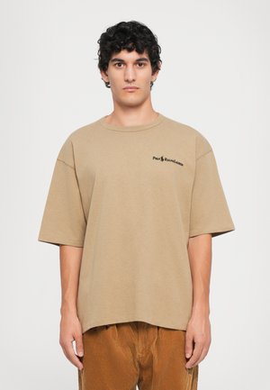 Beige cotton t-shirt with a loose fit, short sleeves, and a round neckline. Features a black logo on the left chest area.