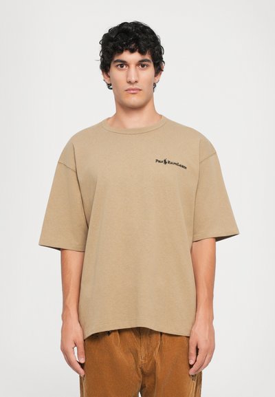 Beige katoenen t-shirt met een losse pasvorm, korte mouwen en een ronde hals. Heeft een zwart logo op de linkerborst.