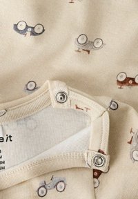 Beżowa tkanina z małymi, powtarzającymi się wzorami zabawek samochodowych i okularów w jasnoszarym i brązowym kolorze. Zapięcie na zatrzask przy dekolcie.