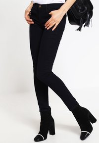 Svarta slim fit-jeans i denim med en slät yta och en åtsittande design. I kombination med svarta ankelboots med vita detaljer.