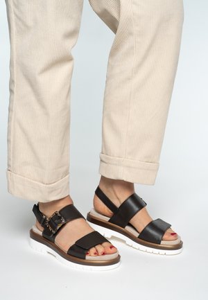 Sandalias de cuero negro con un diseño de dos correas y un detalle de hebilla, con una suela plataforma blanca y detalles visibles de los dedos.