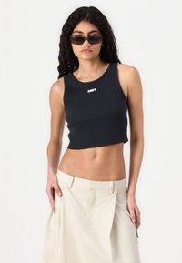 Black cropped tank top with ribbed texture and white "OBEY" logo at the center, paired with light beige cargo skirt, featuring side pockets.