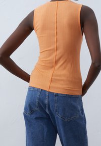 Orange ribbad tanktop med en smal passform och en central sömdetalj. Kombinerad med löst sittande blå denimjeans.