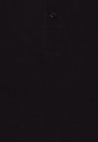 Svart pikétröja med texturerad väv, med en enda knapp vid kragen. Enkelt mönster och enhetlig färg.