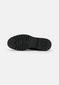 Semelle de chaussure en caoutchouc noir avec un motif de grip texturé, comprenant des crampons profonds et un bord lisse, conçue pour la durabilité et la traction.