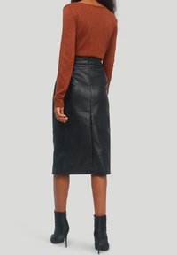 Černá kožená sukně na tužku s vysokým pasem, kombinovaná s rezavě zbarveným topem s dlouhým rukávem a černými kotníkovými botami. Jednoduchý, přiléhavý střih.