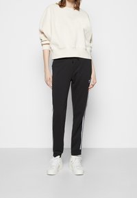 Krämfärgad sweatshirt med avslappnad passform, tillsammans med svarta joggers med vita sidostripes. Vita sneakers fulländar outfiten.