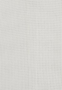Strickstoff in einem strukturierten, hellen Cremeton mit einem gleichmäßigen, gitterartigen Muster; weicher Eindruck mit einem subtilen Glanz.