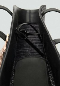 Borsa nera che mostra un interno testurizzato con tessuto intrecciato, una base liscia e manici neri a cerchio. Dettaglio annodato notevole incluso.
