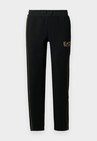 Un pantalon de jogging noir présente un design fuselé, une taille élastique avec cordon de serrage et des rayures dorées le long des côtés et du logo.