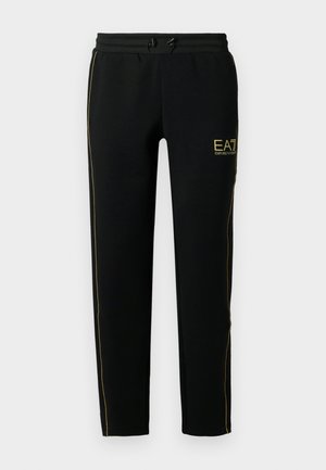 Svarte joggebukser har en tapered design, elastisk midjebånd med snøring, og gullfargede striper langs sidene og logo.