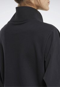 Prenda negra de cuello alto con una textura suave y un ajuste relajado; los detalles incluyen costuras sutiles y un diseño minimalista.