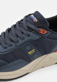 Marineblaue Sneaker mit textilem Obermaterial, Gummisohle, grauen Akzenten, prominenter Markenkennzeichnung und flachen Schnürsenkeln. Verfügt über ein strukturiertes Material und ein gepolstertes Design.