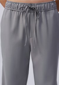 Grijze, lichtgewicht broek met elastische tailleband en trekkoord. Soepele textuur en taps toelopend ontwerp; voorzien van een subtiele voorzak.