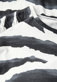 Schwarz-weißer gestreifter Stoff mit weicher Textur, der einen rüschigen Ausschnitt und kontrastierende Farbtöne für Tiefe aufweist. Rundhalsdesign.