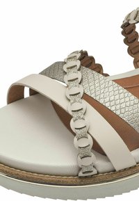 Helle Sandale mit gekreuzten Riemen, ausgestattet mit einem glänzenden silbernen Akzent und einer strukturierten braunen Einlegesohle. Gummisohle sorgt für Grip.