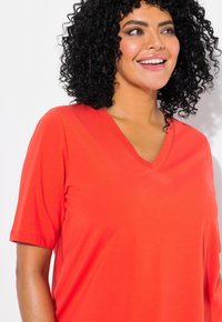T-shirt rosso a scollo a V con maniche corte, in morbido tessuto misto cotone, vestibilità comoda, superficie liscia, braccio parzialmente visibile con tonalità di pelle naturale.