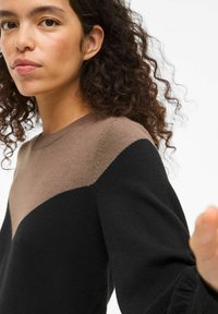 Maglione color-block con tessuto morbido, caratterizzato da una sezione superiore marrone e una sezione inferiore nera, con collo a giro e maniche lunghe.