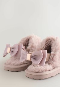 Pantofole rosa fluffy con un ampio fiocco a coste e un accento dorato. Texture morbida e suola in gomma, progettate per comfort e calore.