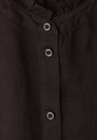 Tissu brun foncé avec une rangée verticale de trois boutons noirs gravés "One Street".