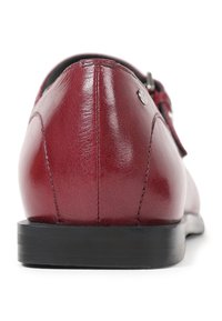 Zapato de cuero rojo con un acabado suave, suela negra y diseño minimalista. Presenta un tacón sencillo y un pequeño detalle metálico.