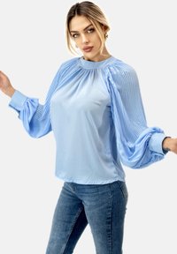 Lichtblauwe blouse met geplooide pofmouwen, ronde halslijn en een gladde stof. Gepaard met slimfit jeans, wat zorgt voor een ontspannen silhouet.