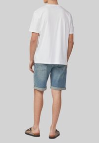 T-shirt en coton blanc, coupe décontractée, associé à un short en denim bleu clair avec des revers. Des sandales décontractées complètent la tenue.