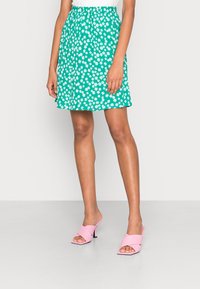 Saia floral verde com padrão de margaridas brancas, cós elástico e um corte solto. Combinada com sapatos de salto baixo cor-de-rosa.