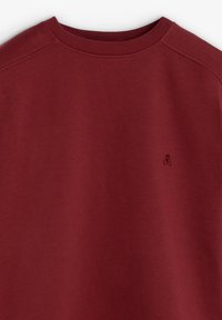 Sudadera burdeos con cuello redondo y mangas raglán. Presenta un sutil logo bordado en la parte frontal, fabricada en algodón texturizado.