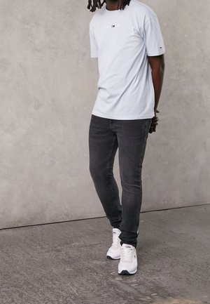 Camiseta de algodón azul claro con mangas cortas y detalle de logo, combinada con jeans oscuros de corte slim y zapatillas blancas con acentos oscuros.