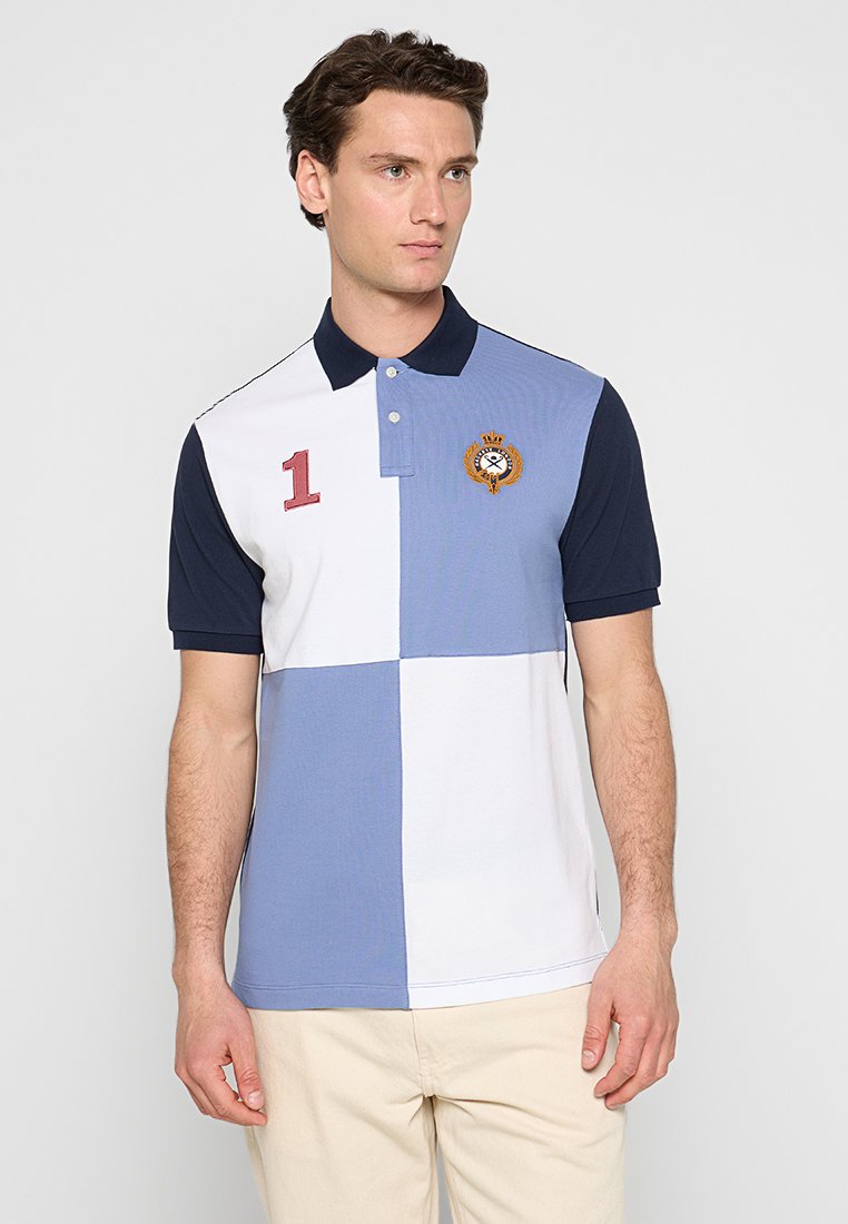 Polo shirt avec un design en coloris bloc comprenant des sections bleu marine, blanc et bleu clair. Accent brodé notable avec le numéro 1 sur la poitrine.