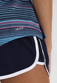 Top deportivo a rayas azul y negro con detalles en rosa y logotipo plateado, combinado con pantalones cortos marinos con ribetes blancos y aberturas laterales.