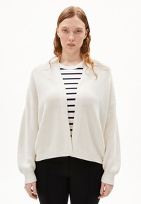 Lightweight, textured cream cardigan with dropped shoulders and a V-neck, paired with a black-and-white striped top beneath.