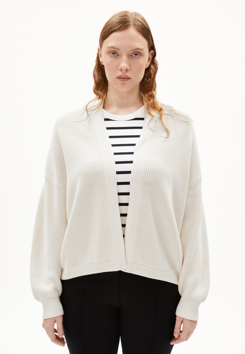 Lightweight, textured cream cardigan with dropped shoulders and a V-neck, paired with a black-and-white striped top beneath.