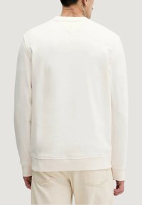 Krämfärgad sweatshirt med rund halsringning, ribbad nederkant och ärmslut med mudd. Har en slät, mjuk yta på baksidan utan synliga logotyper.