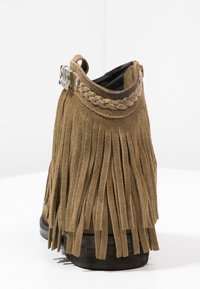 Brązowe zamszowe botki za kostkę z frędzlami, plecionym paskiem i srebrnymi zdobieniami. Płaska podeszwa, teksturowana cholewka oraz okrągły nos.