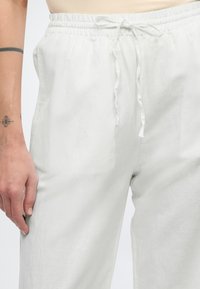 Vita, löst sittande byxor med elastisk midja och dragsko. Tyget verkar vara lätt och ha en slät textur.