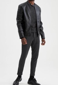 Veste en simili cuir noir avec détails côtelés aux épaules, associée à un pull gris et un pantalon de jogging gris foncé. Une paire de chaussures noires complète la tenue.